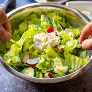 Lithuanian summer garden salad being mixed with sour cream in a large metal bowl.