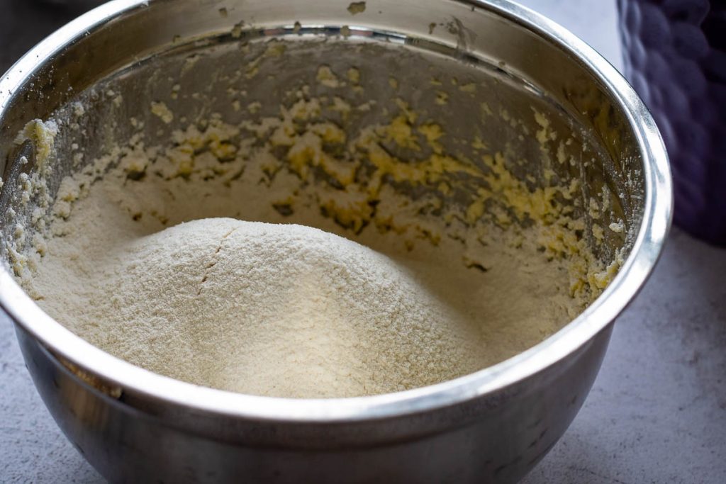 Dry ingredients siften on top of the butter and egg mixture in a metal bowl.