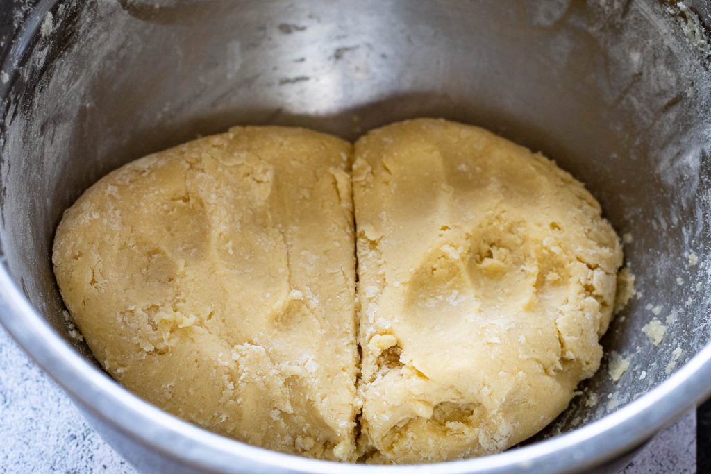 The sugar cookie doug hdivided into two in a metal bowl.