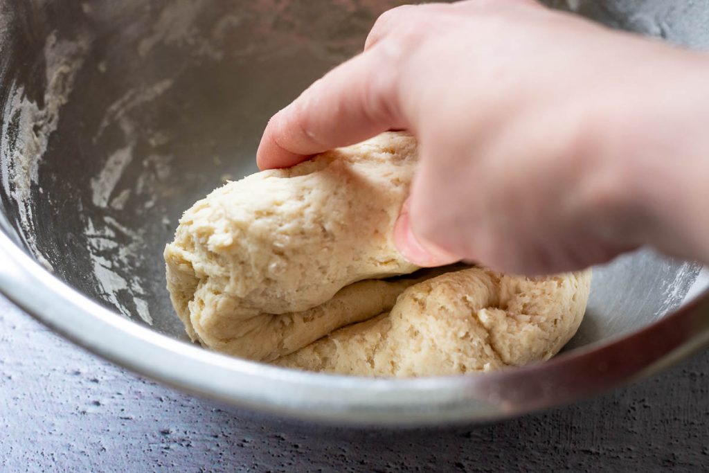 Bridning the dough into a ball in a metal mixing bowl.
