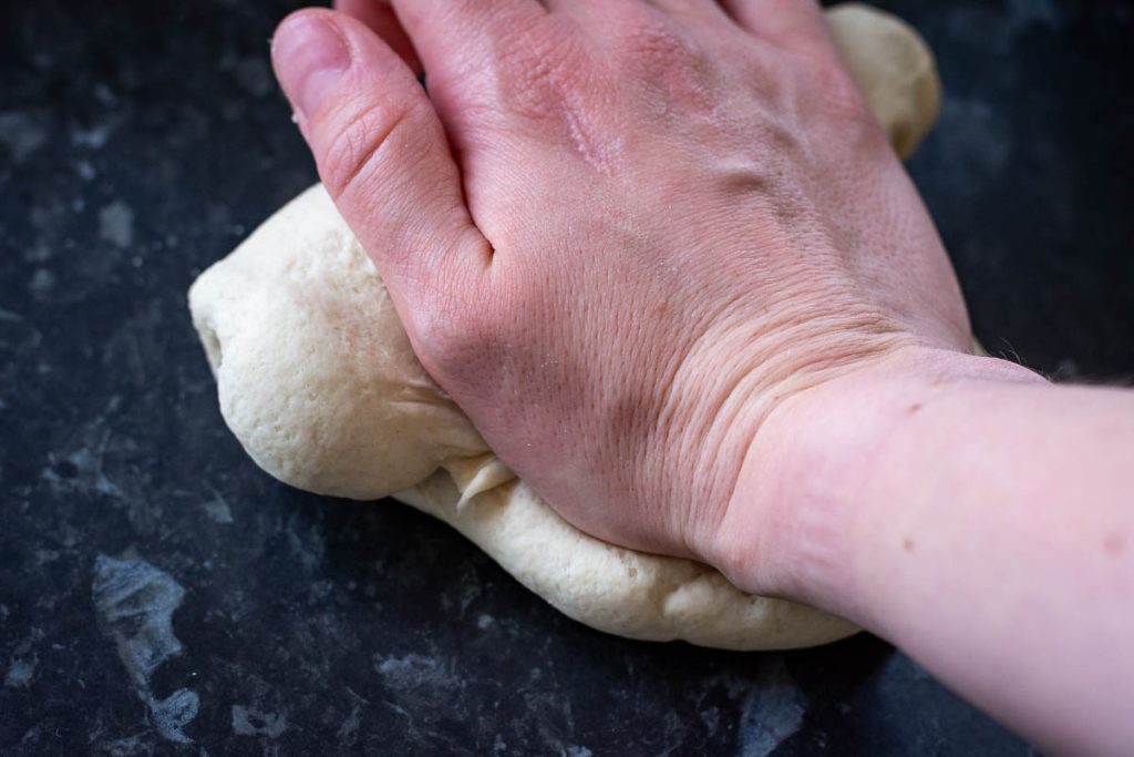 Kneading the Lithuanian flour dumpling dough on a dark kitchen surface.