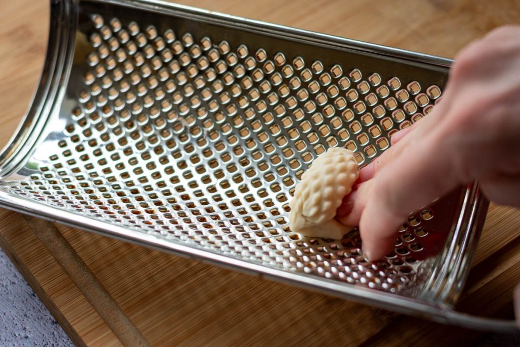 pressing a piece of dough into the inside of a star grated to create spikes on the dumplings.