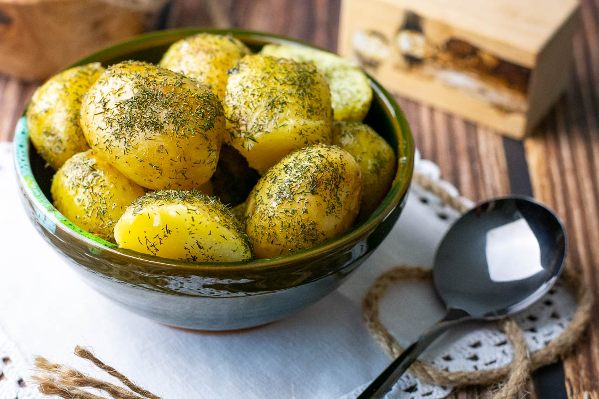 Boiled potatoes with dill and butter in a small green bowl served as a side dish.