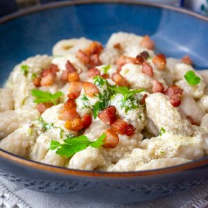 Lithuanian boiled flour dumplings, known as Miltiniai Ežiukai, served with thin sour cream sauce and crispy bacon on top.