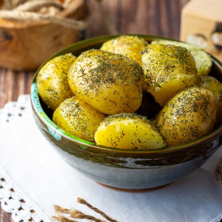 Boiled potatoes with dill and butter in a small green bowl served as a side dish.