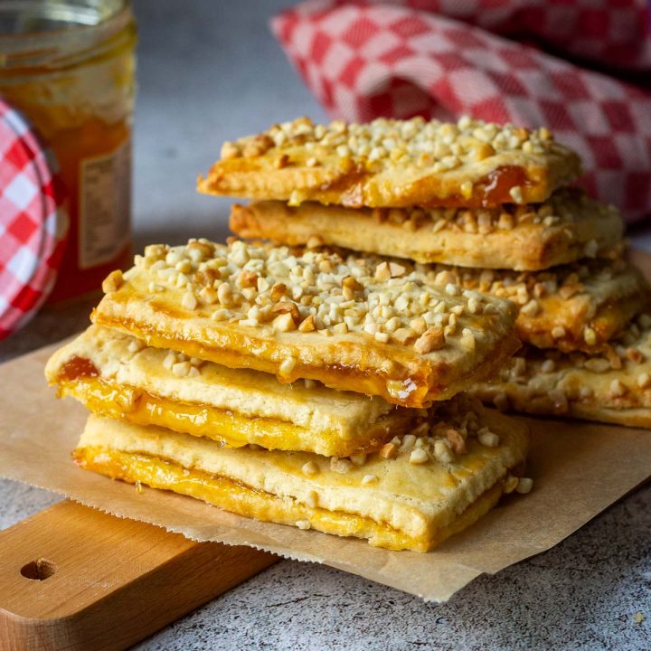 A stack of Lithuanian Jam-Filled Sugar Cookies with nut topping on a wooden board.