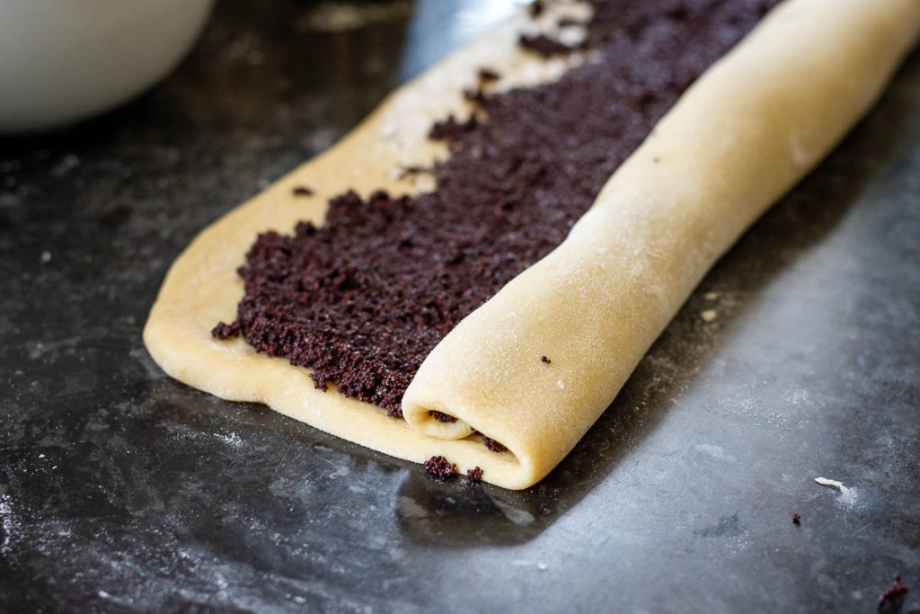 The poppy seed filling spread onto the dough and being shaped into a tight roll. 