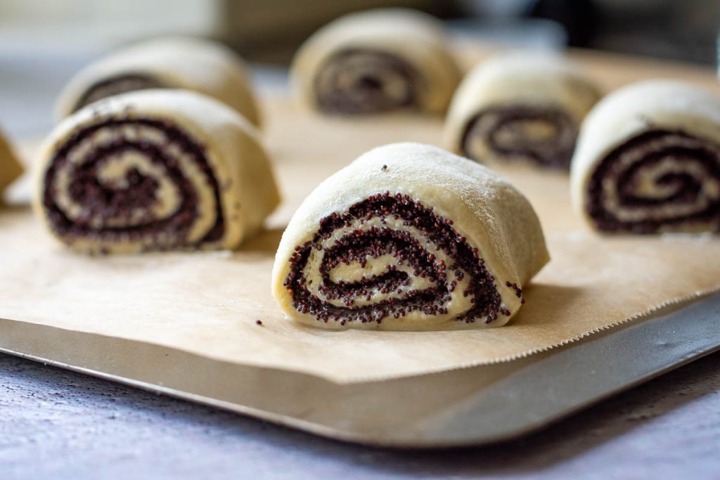 Lithuanian poppy seed buns arranged on a baking sheet lined with parchment paper. 