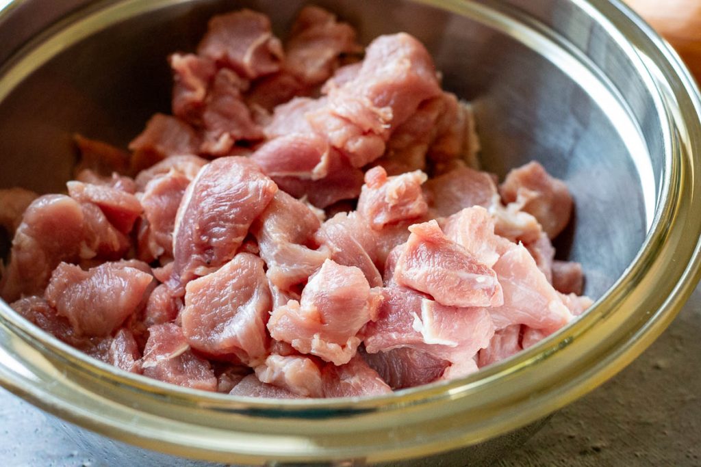 Pork shoulder cut into cubes in a metal bowl.