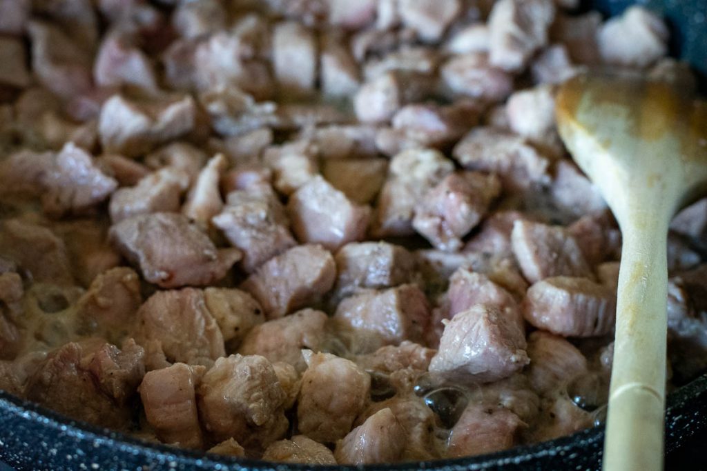 Pork pieces browning in a frying pan.