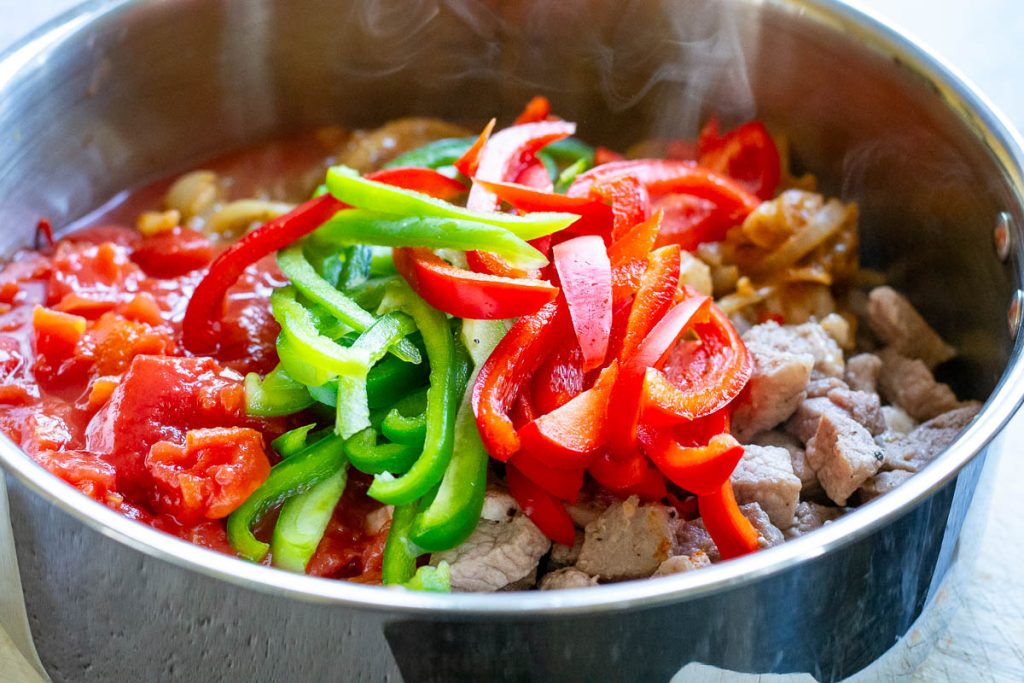 Browned pork, sliced bell peppers and canned tomatoes added to the onion pot.
