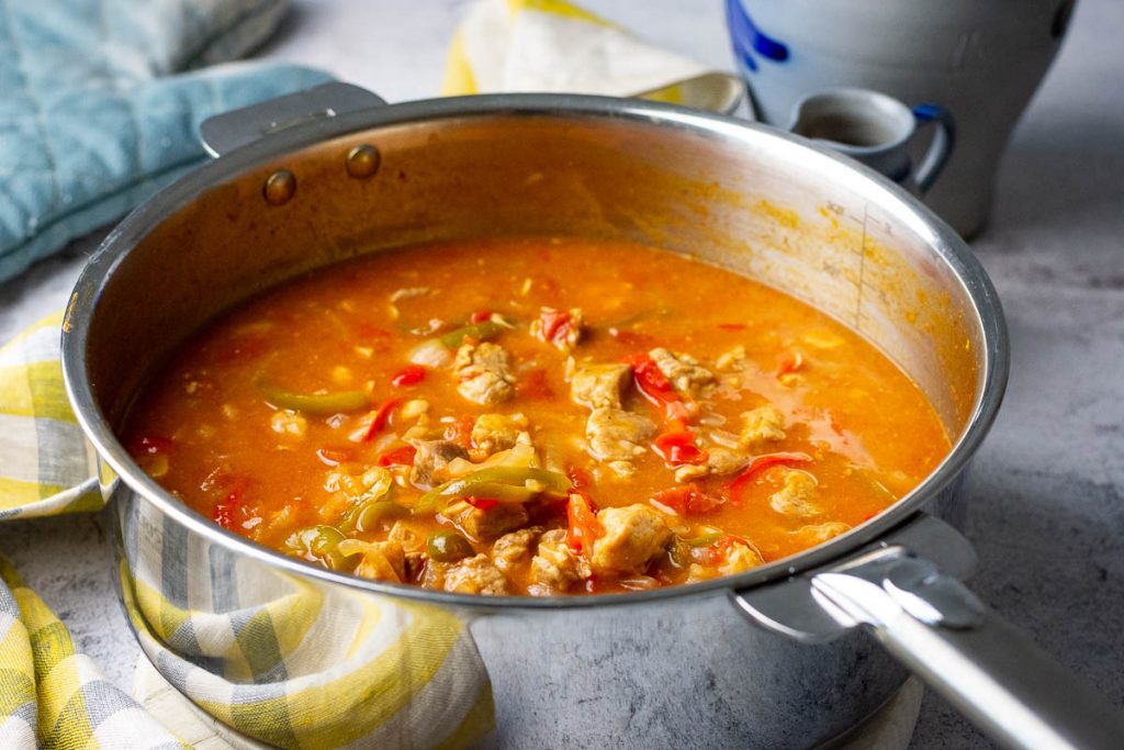 Lithuanian pork goulash in a large stainless steel pan set on a wooden board.