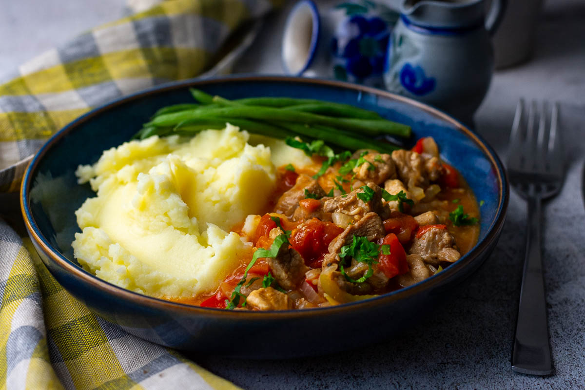 Lithuanian Pork Goulash served with mashed potatoes and green beans in a blue bowl.