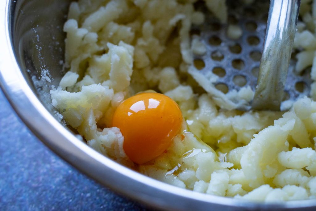 Mashed boiled potatoes with an egg on top and a potato mashed to the side.