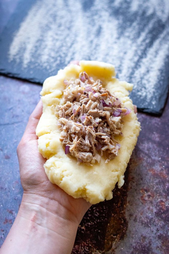 Flattened potato dough with pork filling in the centre in the palm of a hand.