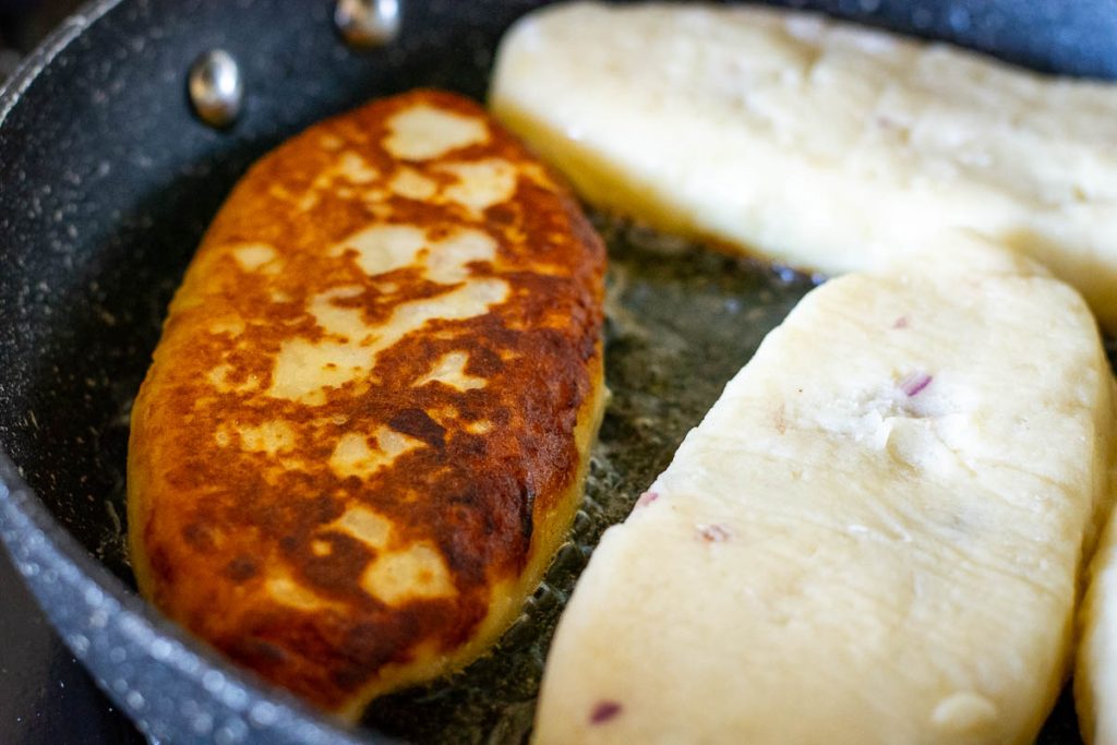 Samogitian pancakes frying in butter and oil in a large pan.