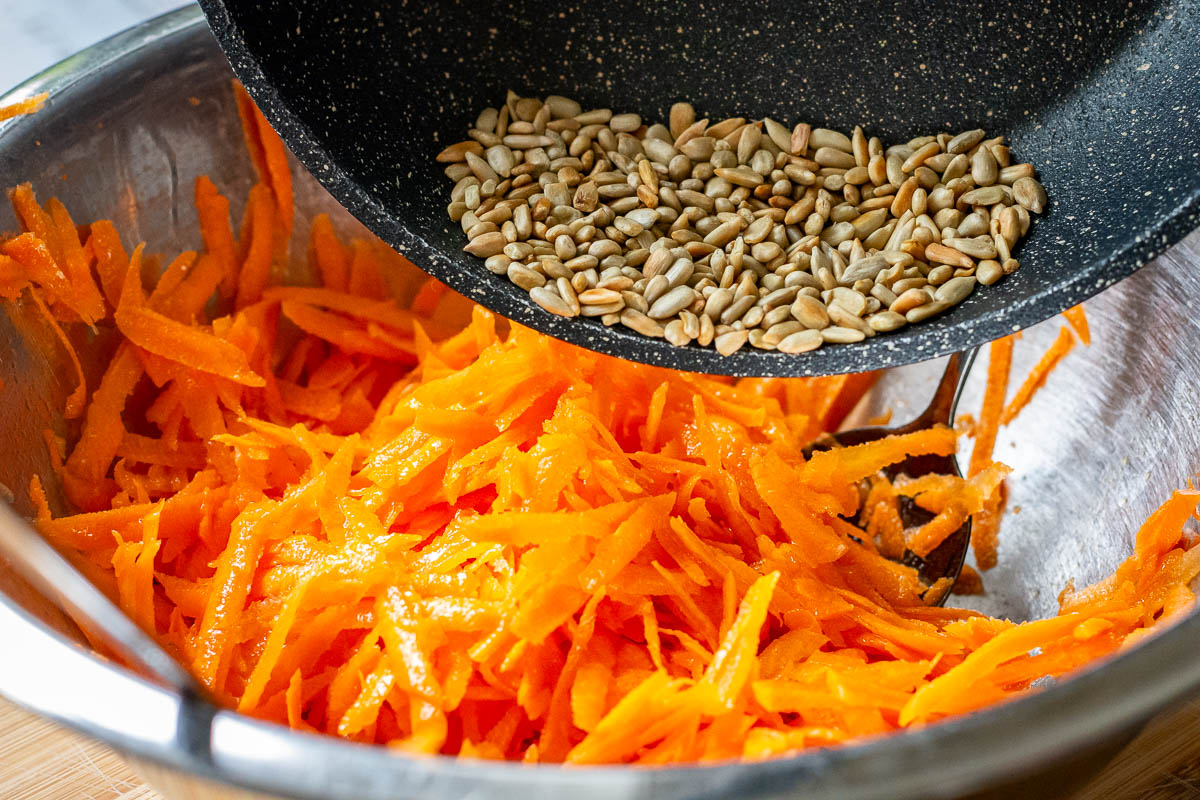 Adding toasted sunflower seeds to grated carrots.