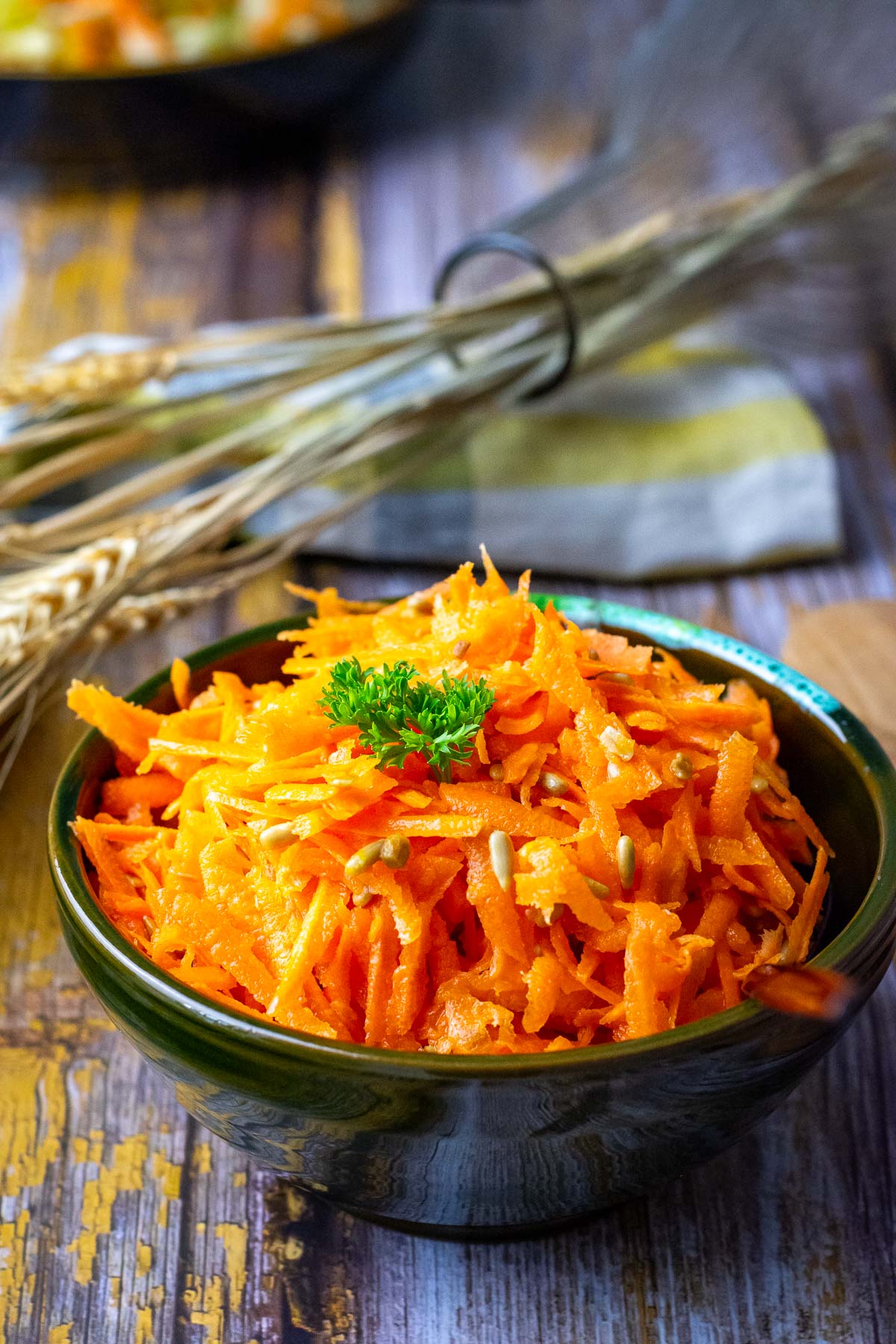 Lithuanian Carrot Salad With Sunflower Seeds in a small dark bowl garnihsed with parsley.