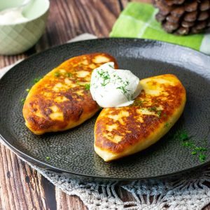 Lithuanian potato pancakes stuffed with meat on a black plate with sour cream.