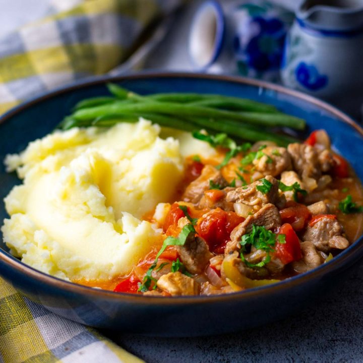 Lithuanian Pork Goulash served with mashed potatoes and green beans in a blue bowl.