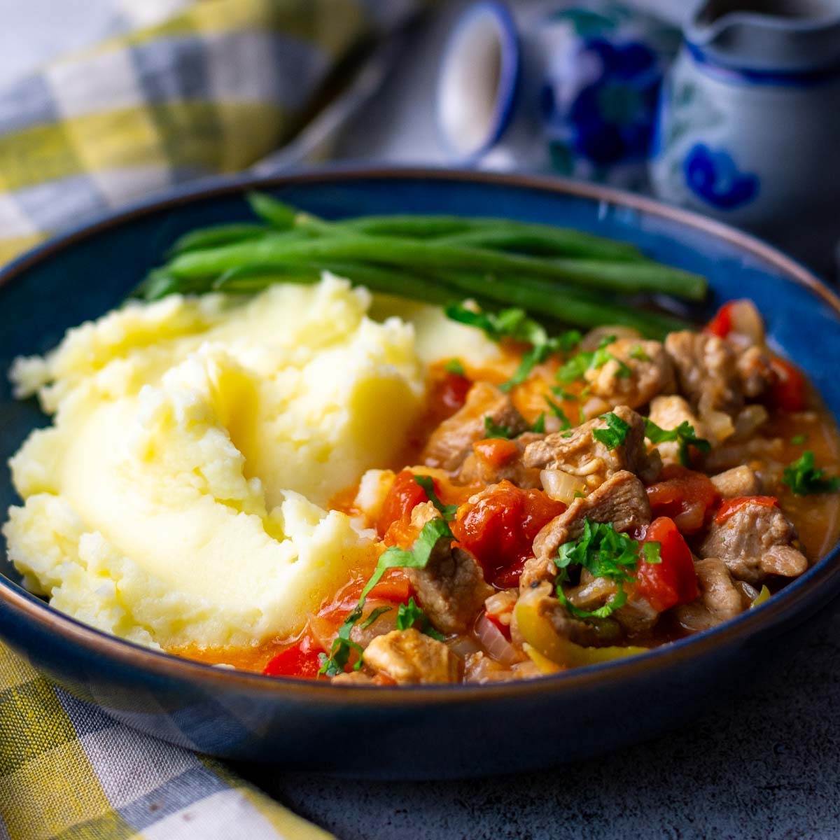 Lithuanian Pork Goulash served with mashed potatoes and green beans in a blue bowl.