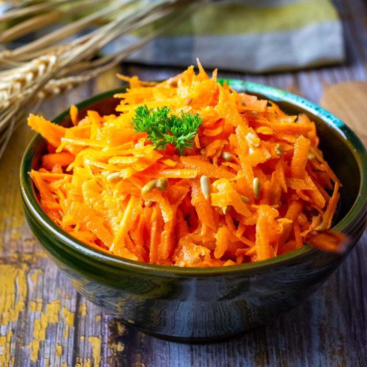 Lithuanian Carrot Salad With Sunflower Seeds in a small dark bowl garnihsed with parsley.