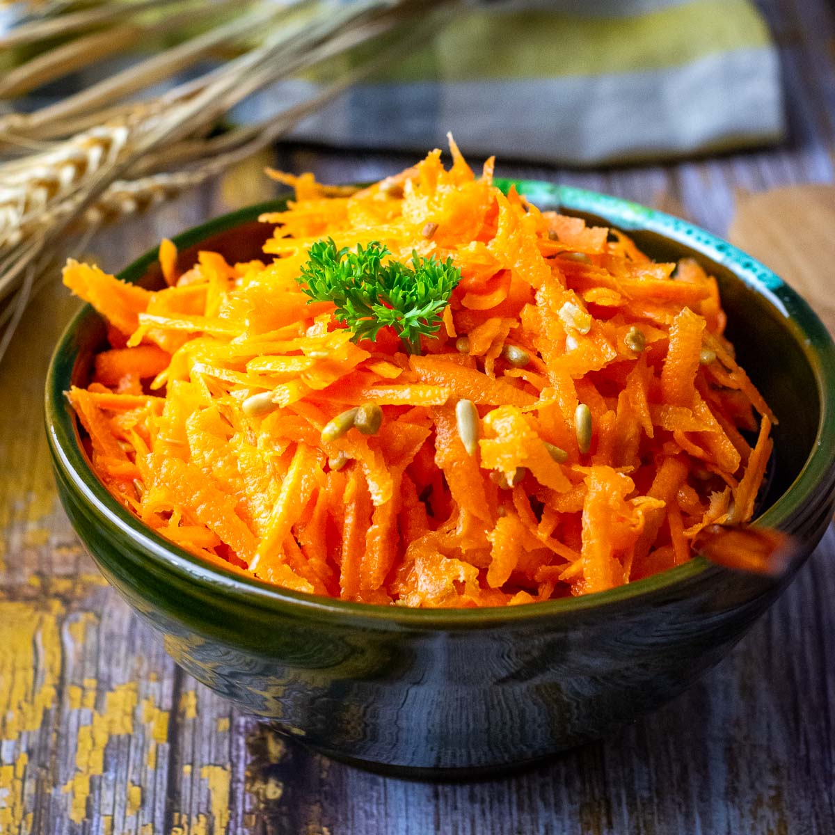 Lithuanian Carrot Salad With Sunflower Seeds in a small dark bowl garnihsed with parsley.