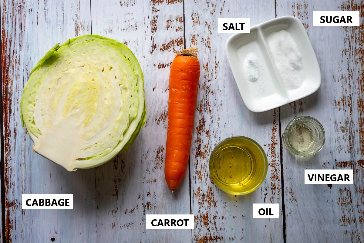 Ingredients for Lithuanian cabbage and carrot salad on a white wooden table.