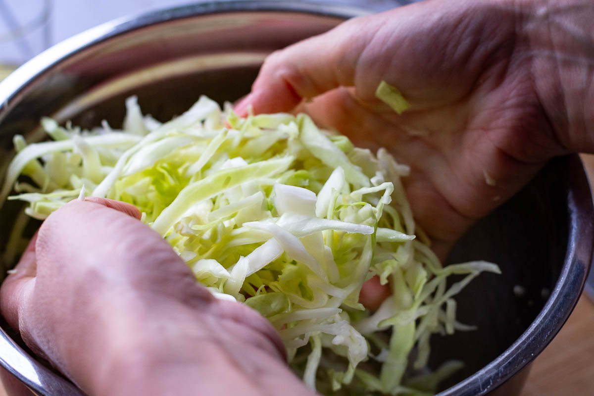 Massaging cabbage in a bowl to soften it.