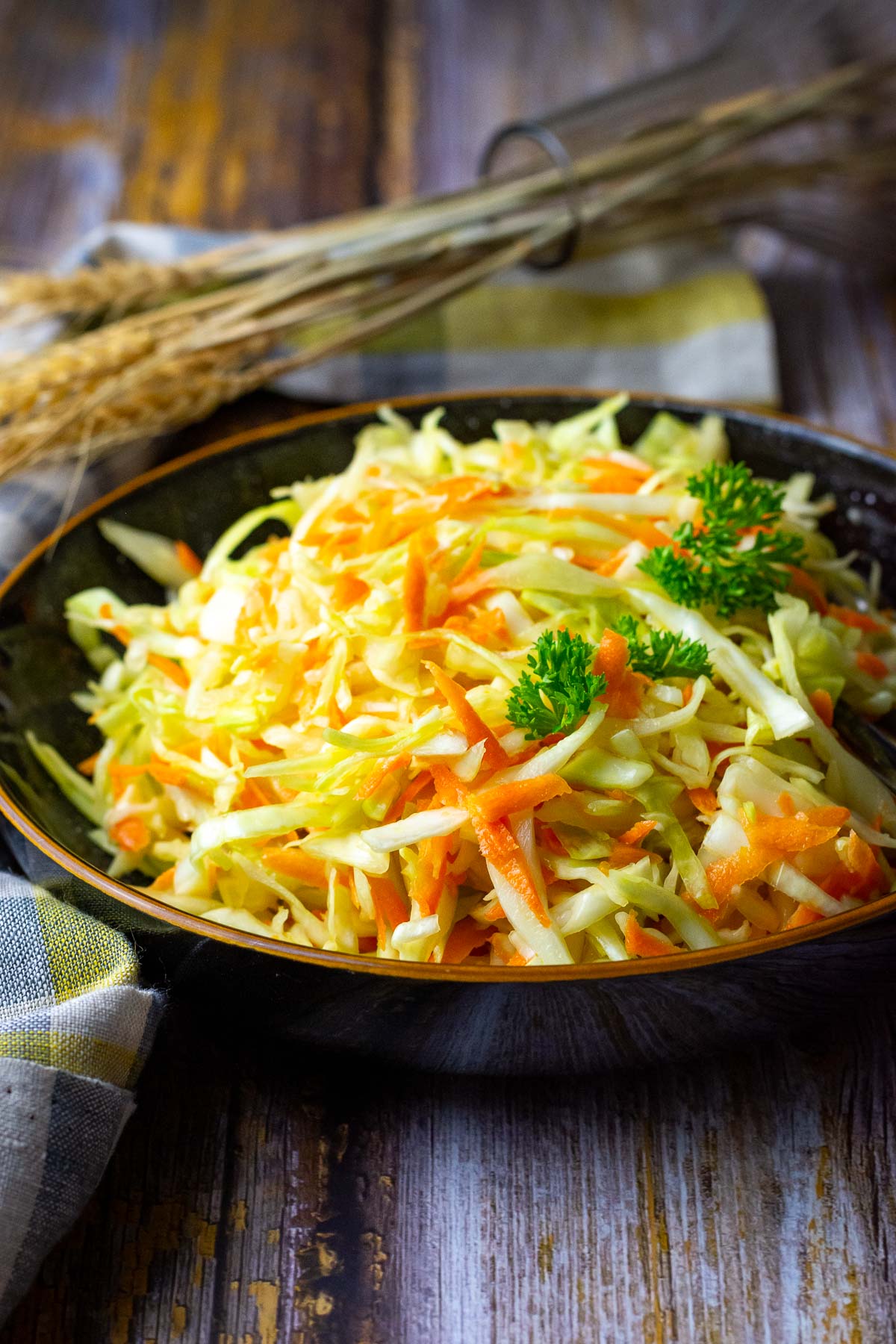 Lithuanian cabbage salad served in a black bowl with a brown rim, garnished with parsley.