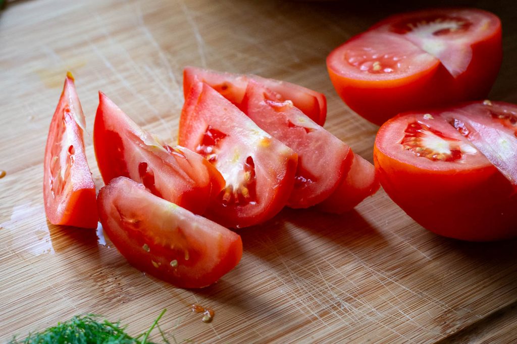 Tomatoes cut into wedges on a wooden chopping board.