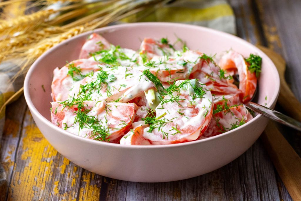 Lithuanian tomato salad is served in a pink bowl on a wooden table.