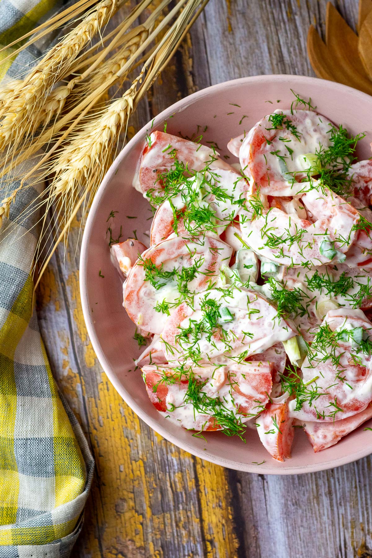 Lithuanian tomato salad is served in a pink bowl on a wooden table.
