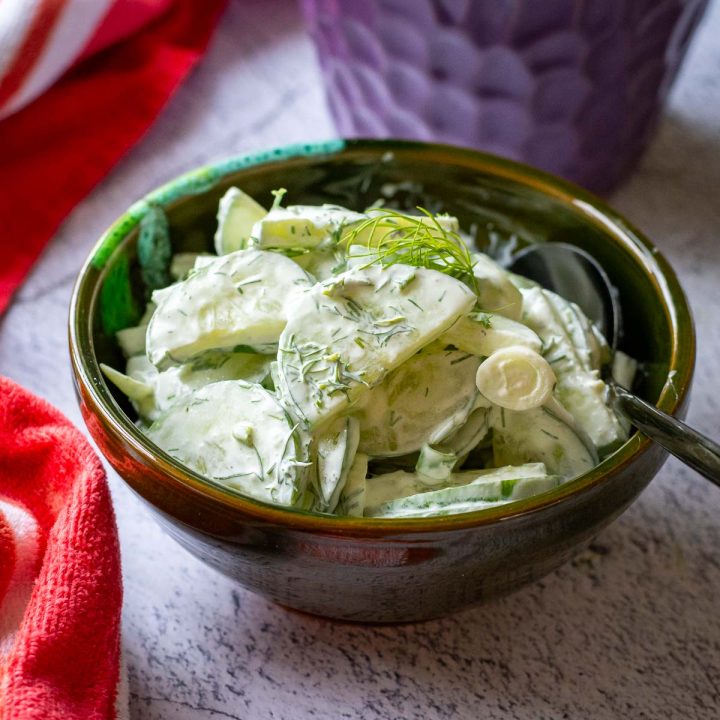 Lithuanian Cucumber salad with dill and sour cream in a small dark green bowl.