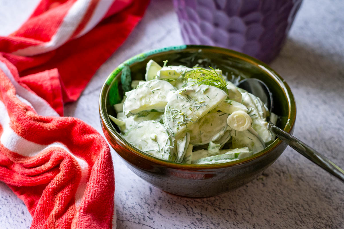Lithuanian Cucumber salad with dill and sour cream in a small dark green bowl.
