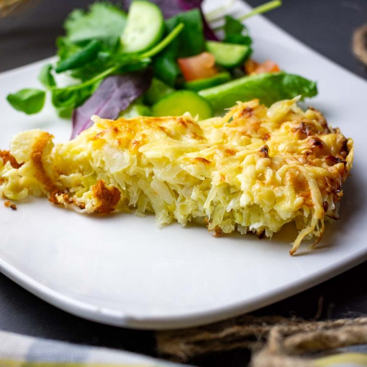 A slice of cabbage casserole with cheese topping on a plate with a side salad.