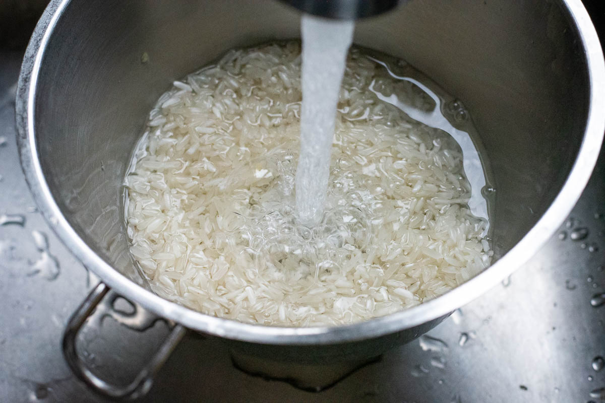 Running cold water through cooked rice in a colander.