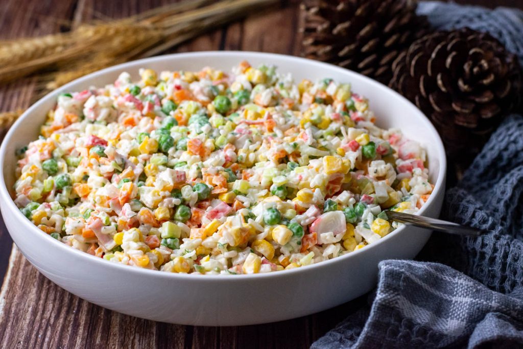 Lithuanian salad with crab sticks and rice in a large white bowl on a wooden table.