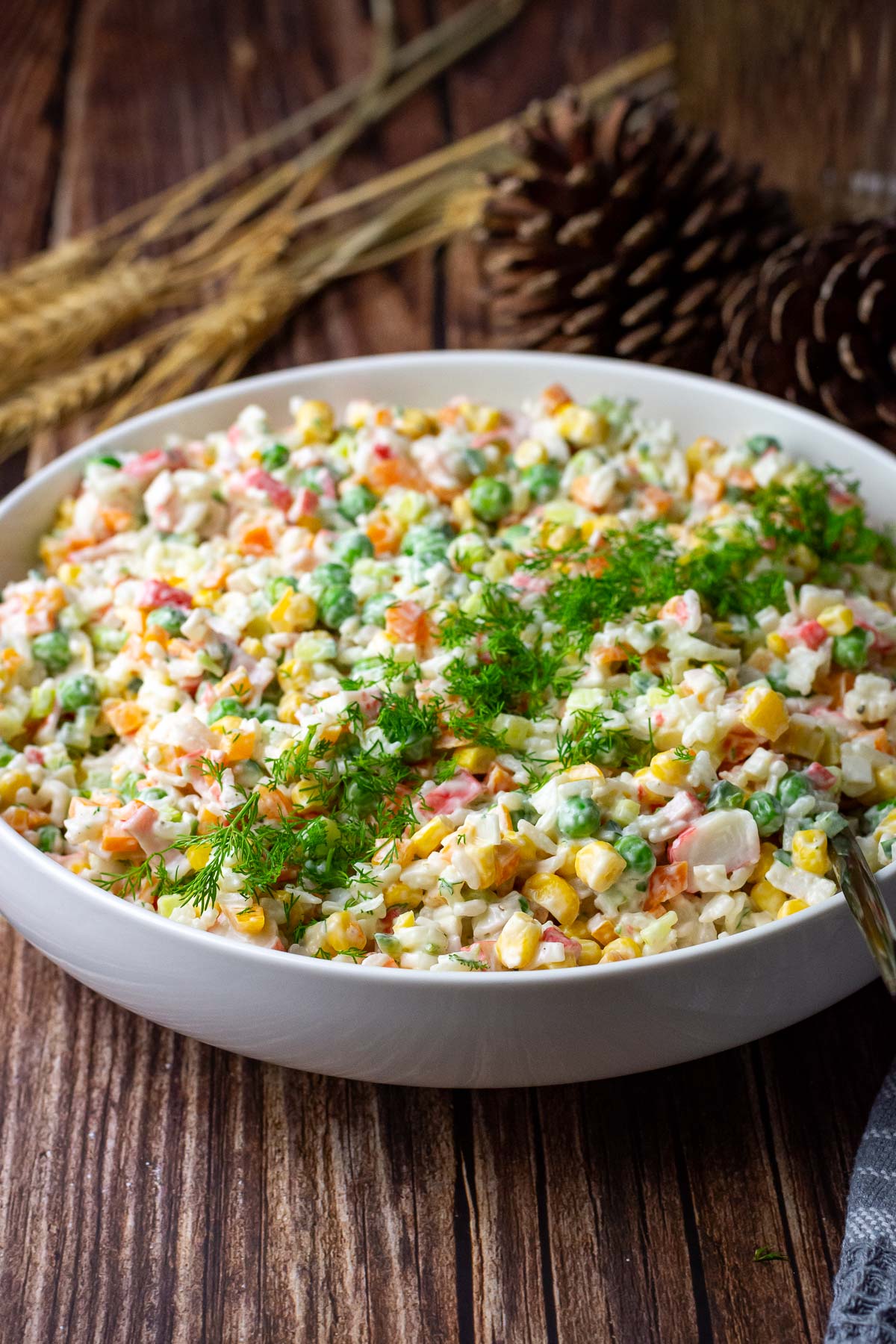 Lithuanian rice salad with crab sticks in a lrge white bowl garnished with fresh dill.