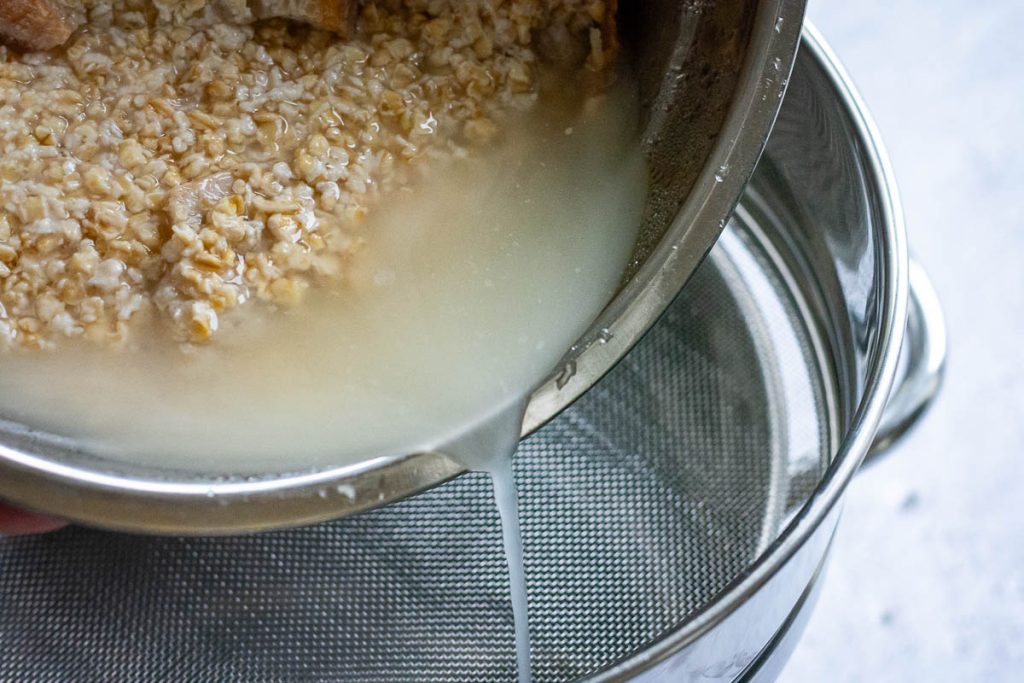 Pouring the fermented oat liquid through a sieve into the pot.