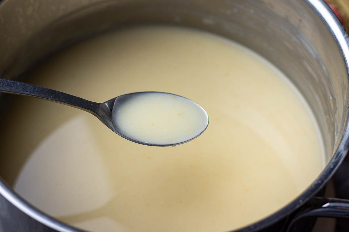 Fermented oat drink in a large pot with one spoonful lifted out of it.
