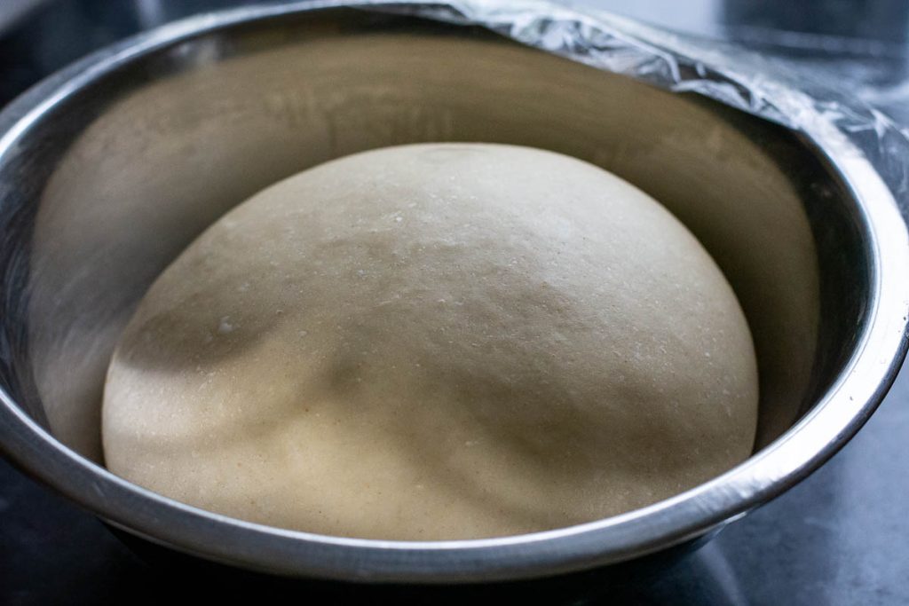 Sweet dough for the buns in a metal bowl after proofing.