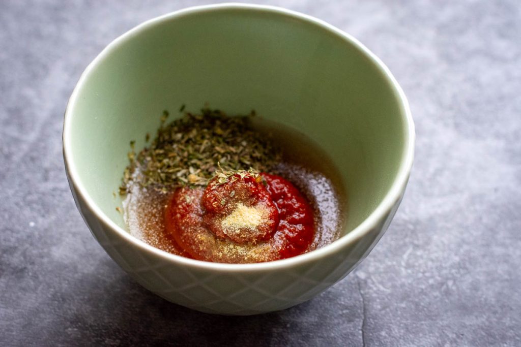 Tomato puree mixed with water, herbs and garlic powder in a small green bowl.