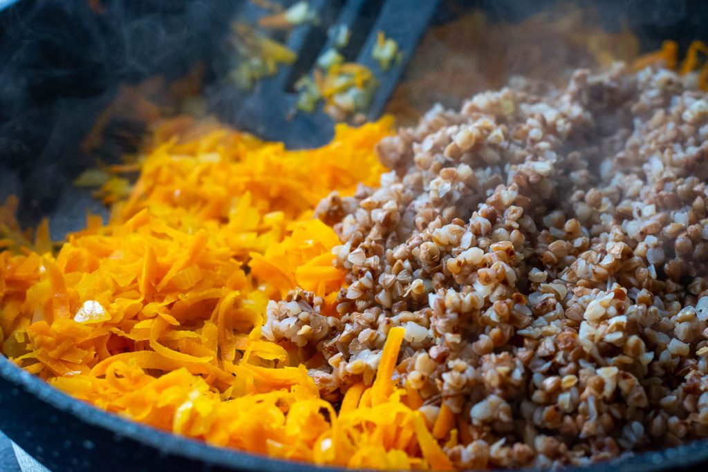 Sauteed carrots and onions with boiled buckwheat in a pan.
