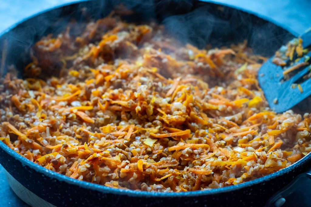 Sauteed carrots and onions with boiled buckwheat in a pan.