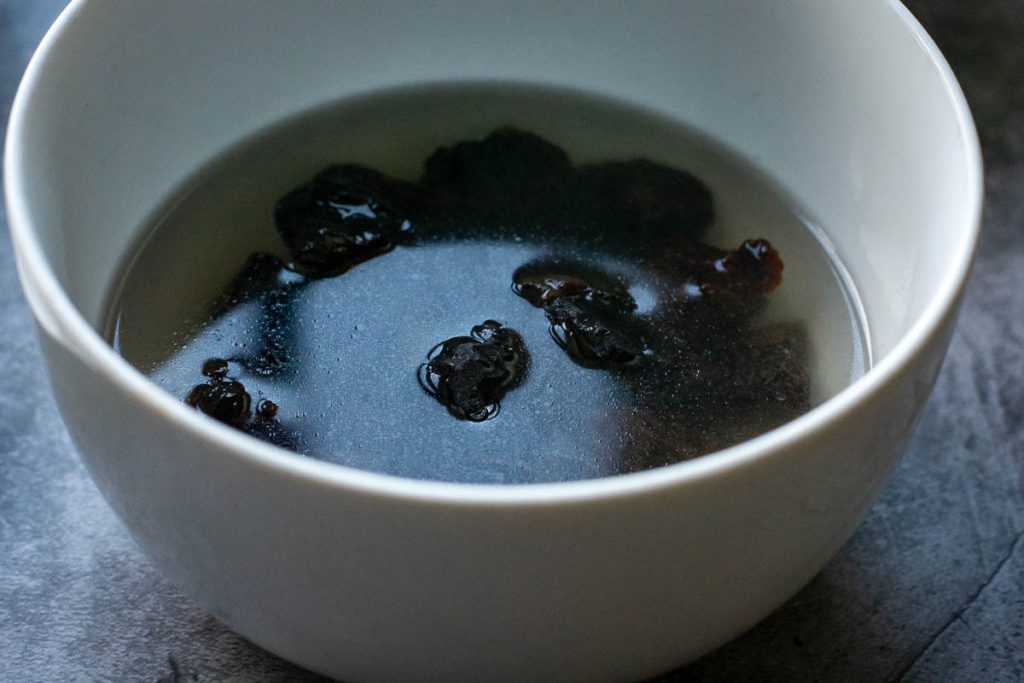 Soaking prunes in hot water in a white bowl.