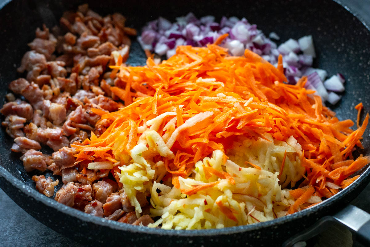 Vegetables sauteeing in a pan with bacon.