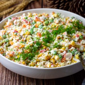Lithuanian rice salad with crab sticks in a lrge white bowl garnished with fresh dill.