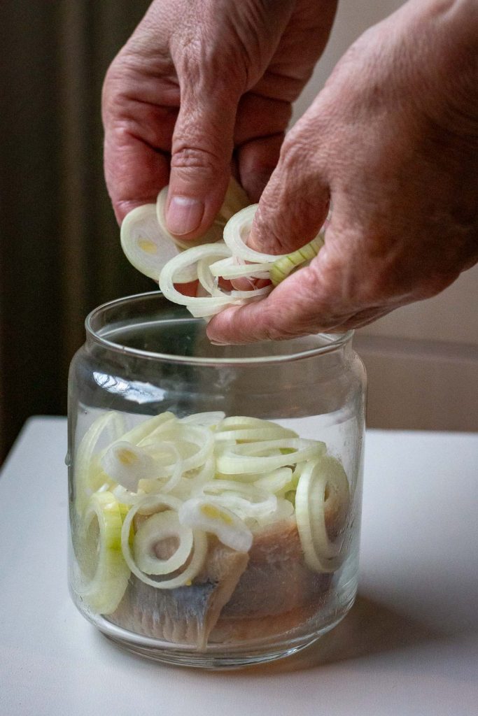 Onion rings being placed in a jar with the herring fillets.