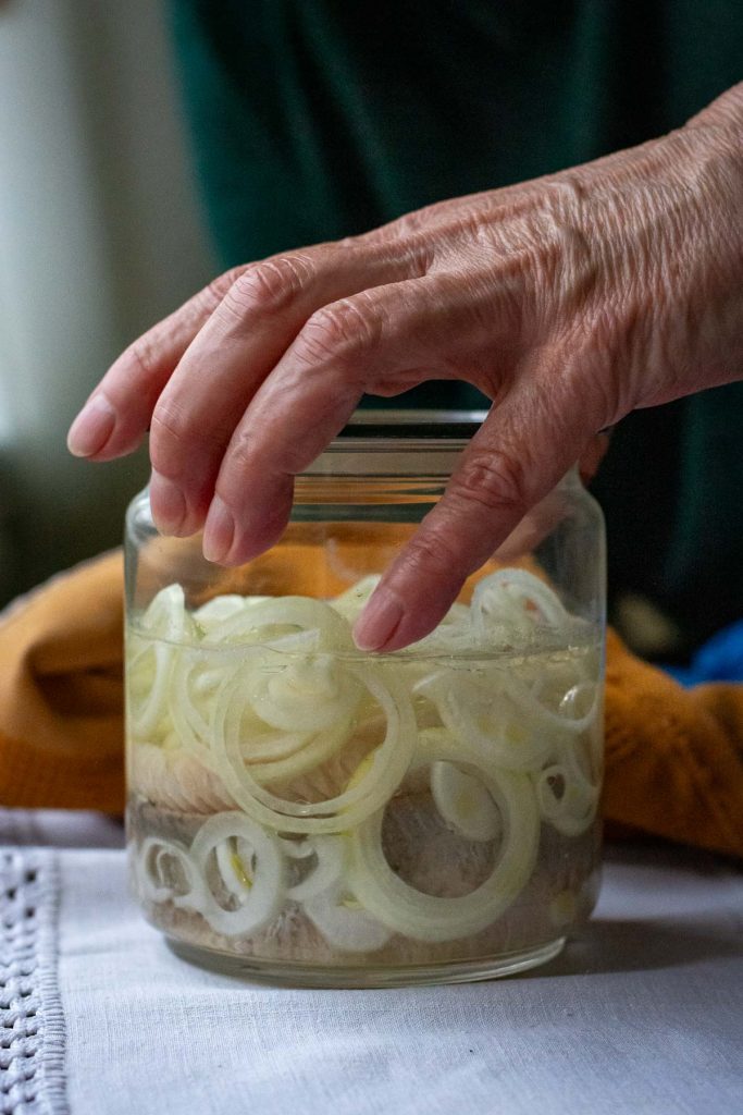 A jar with herring and onions in pickling liquid being closed with a lid.
